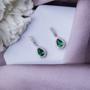 A pair of sterling silver drop earrings with green gemstones, displayed on a white surface with a floral background.